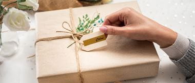 En hånd holder i en merkelapp som er festet til en gave med bånd og brunt papir