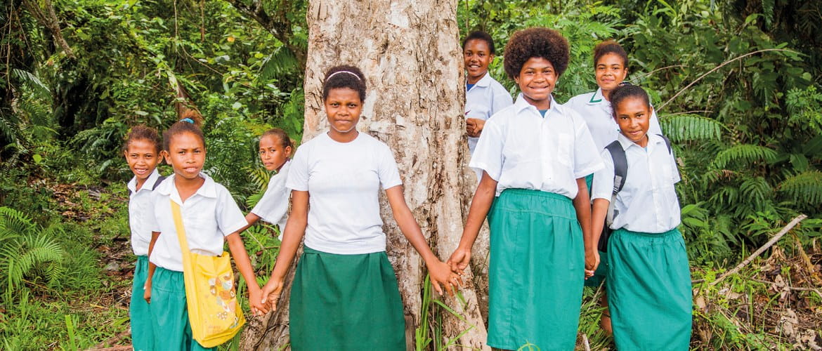 A group of eight students from a Brother and Cool Earth funded community scholarship pose next to a tree in a forest in Orangerie Bay, Papua New Guinea