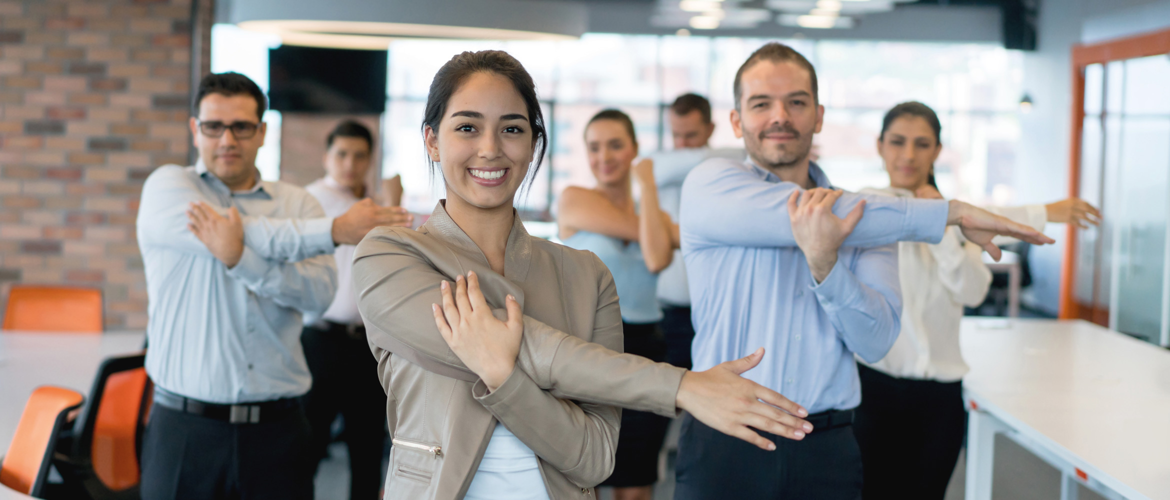 Seven office co-workers take time out to focus on fitness and wellbeing by doing some stretching exercises together in the workplace of the future