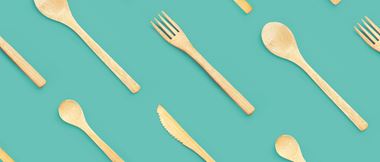 Environmentally friendly sustainable bamboo wooden cutlery (knife, fork and spoon) are lined up against a teal solid background