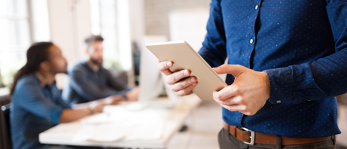 Man using tablet with people discussing work on table behind him