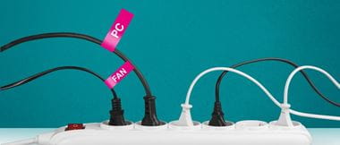 A multi-plug extension in the office has a variety of electrical devices plugged in. Only two of the five are brightly labelled with a bright pink label. They clearly identify a 