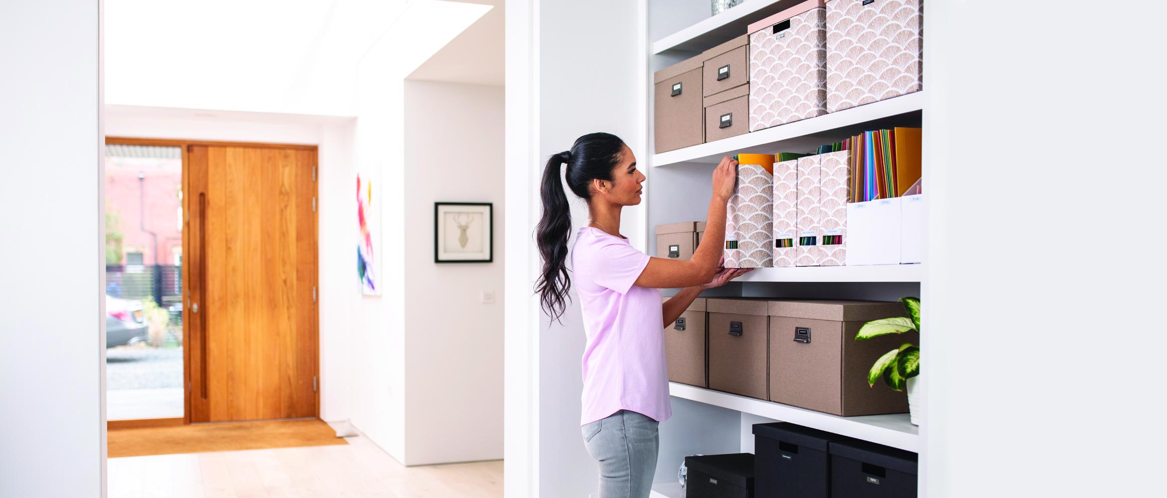 A female staff member is working from a home office / hybrid working. She is organising her paper files using a labelling printer to increase business productivity.