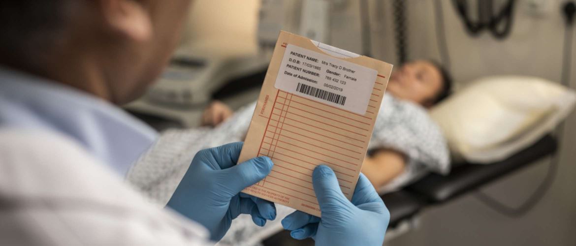 En lege undersøker en pasientmappe som har en trykt etikett med strekkoder og pasientopplysninger