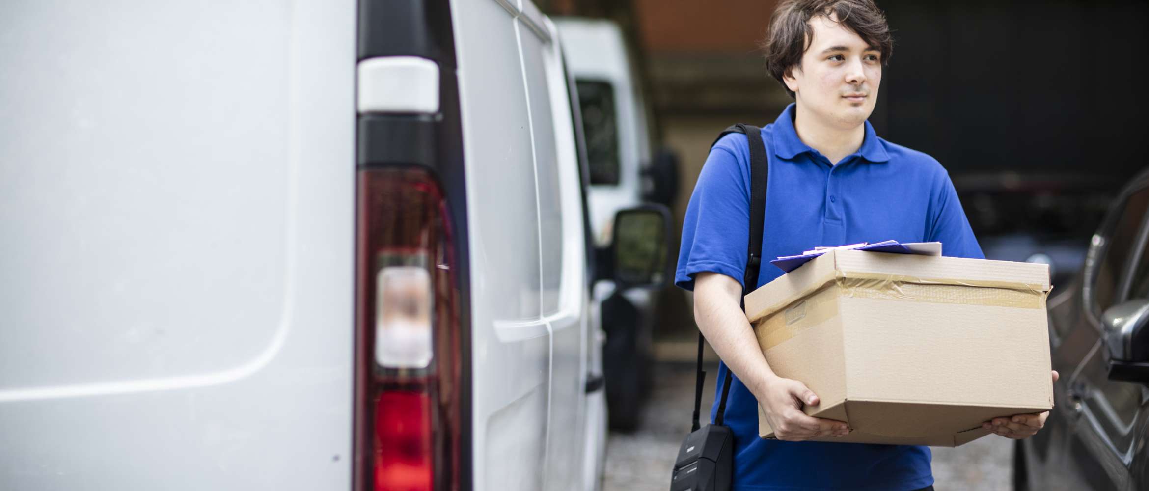 A male delivery driver is holding a cardboard box