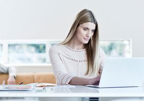 En kvinne sitter ved et bord med en datamaskin