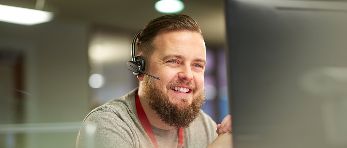 Smiling man talking on a hands free headset and looking at a computer screen