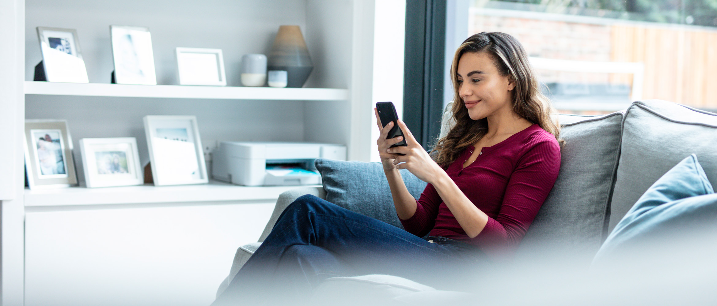 Kvinde med en mobiltelefon i hånden, der sidder i en sofa