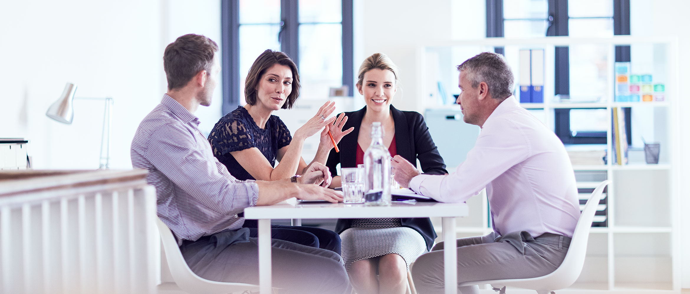 Four colleagues talking and smiling in an office setting