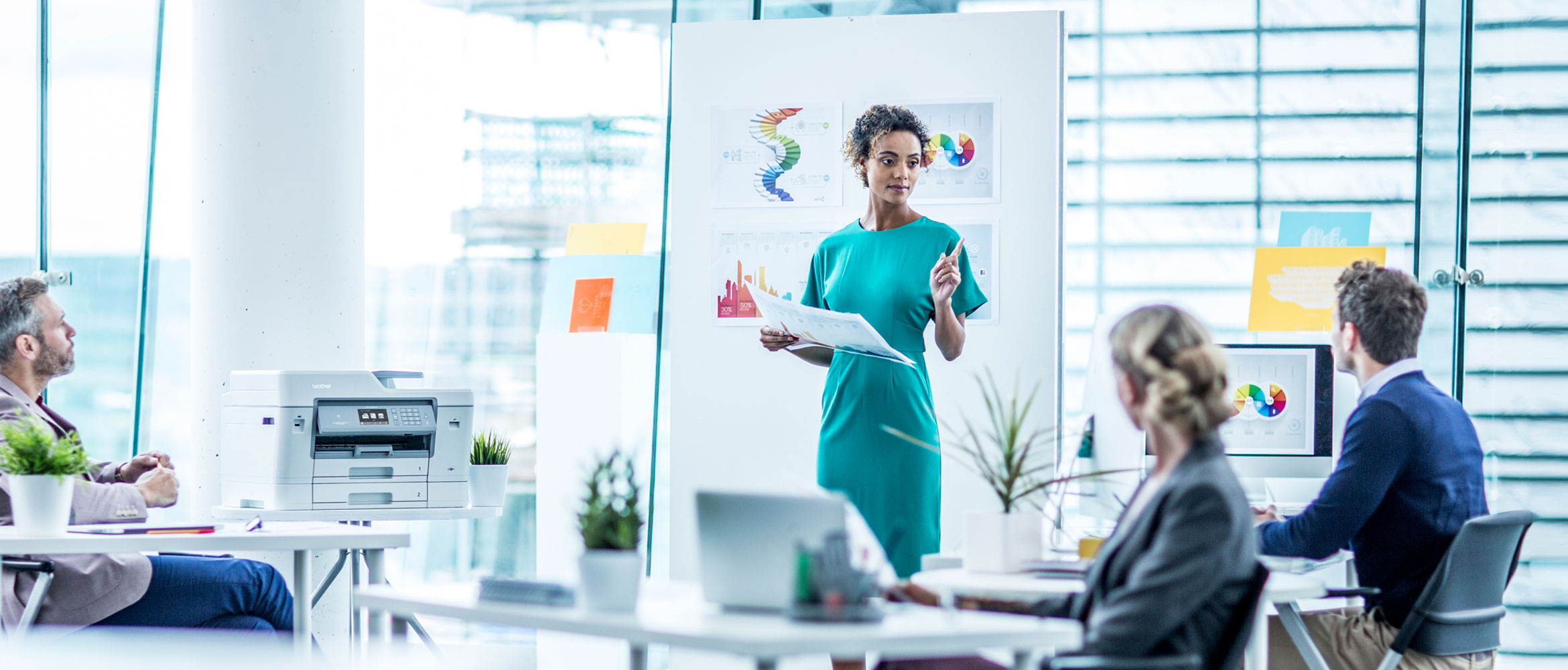 A woman standing in front of a mood board addressing three colleagues 