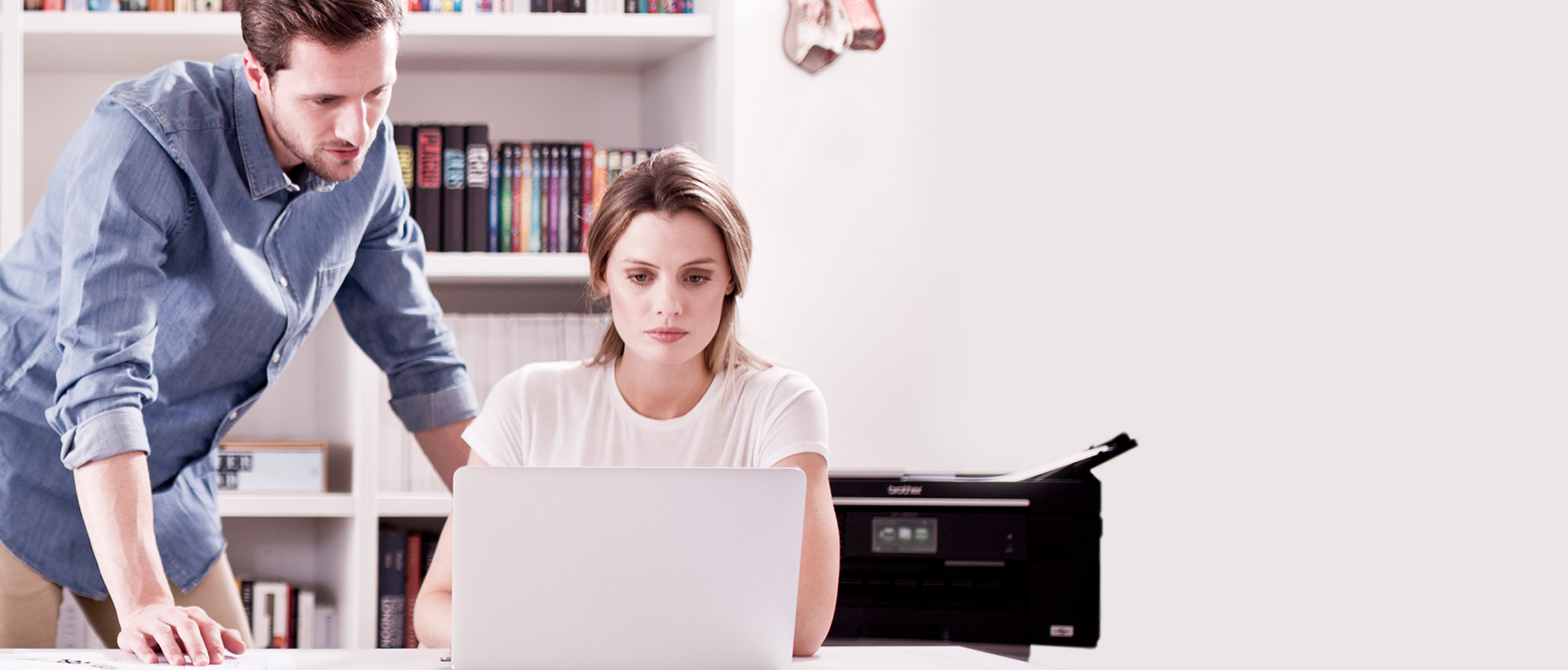 Man and woman collaborating on a laptop and concentrating, with a Brother printer behind them