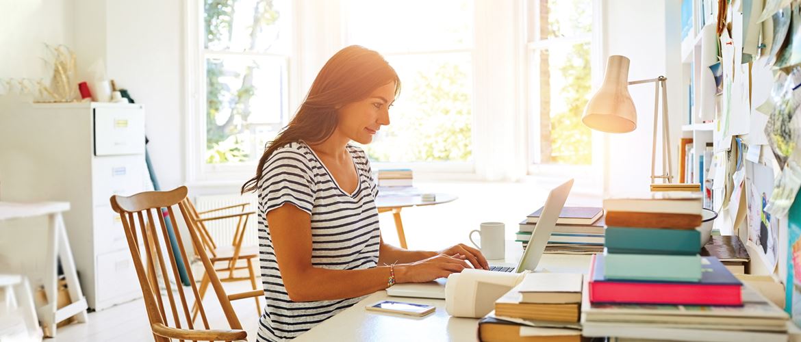 žena u prugastoj majici za stolom s prijenosnim računalom, bijelim namještajem, šarenim mapama