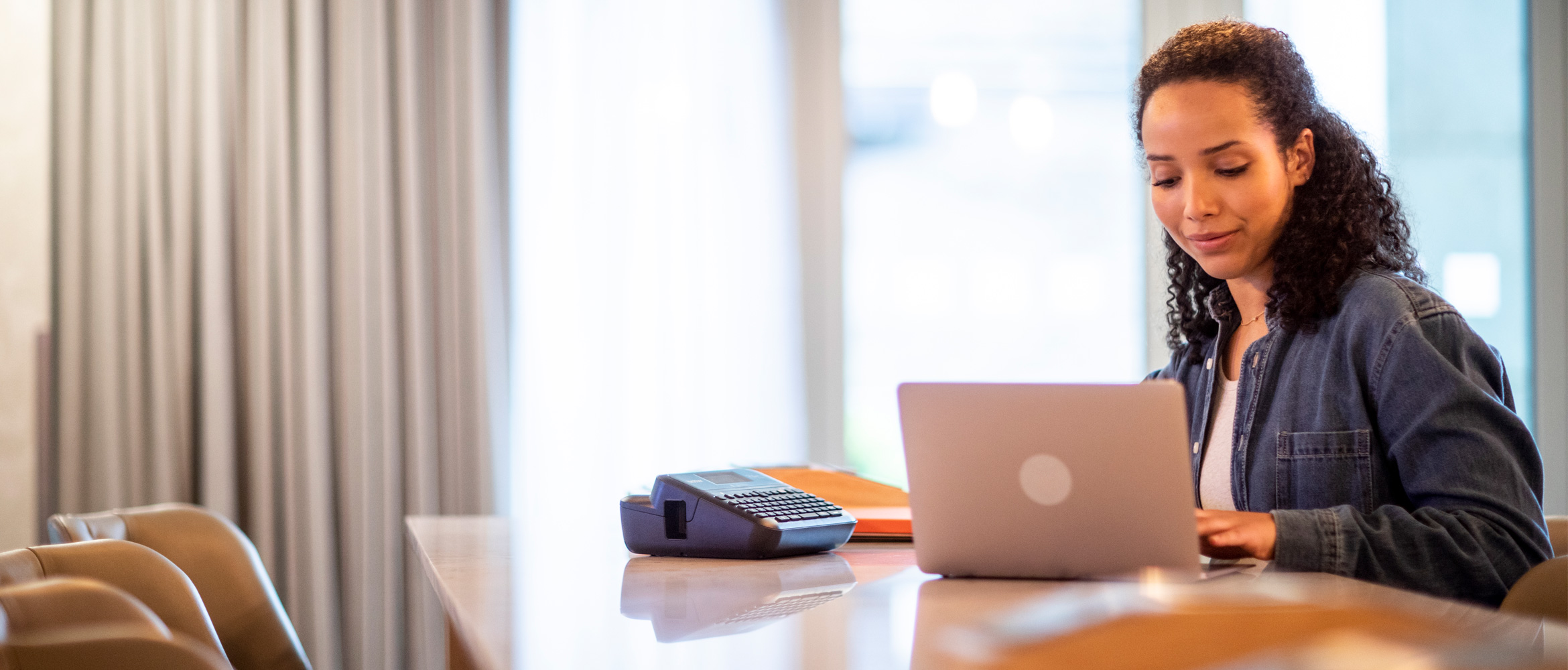 woman sat in coworking space with ptouch label printer beside laptop 