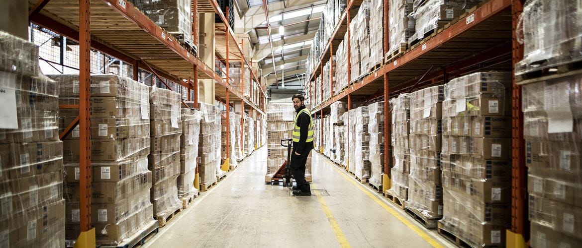 Man in high visibility vest pulling a pallet along warehouse aisle