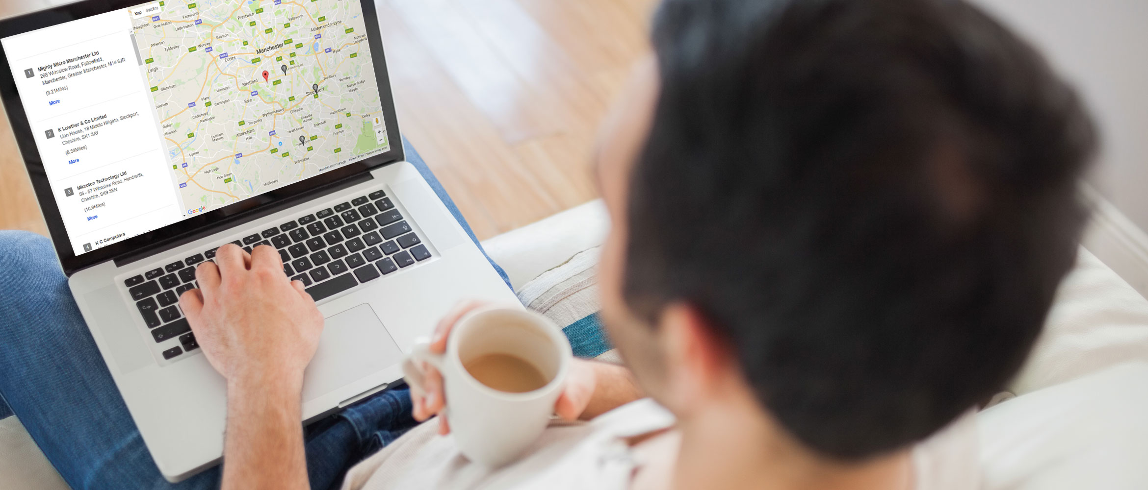 Man sat on a sofa, drinking tea searching for Brother Service Centre on computer