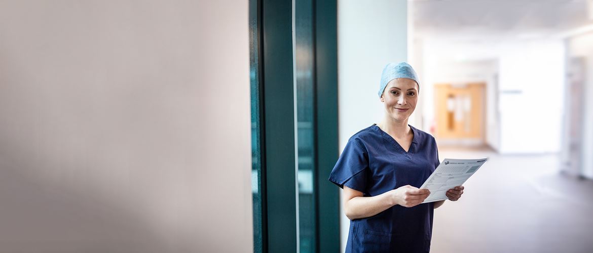 Female doctor wearing surgical scrubs and hat holding blue folder, in corridor with door in background