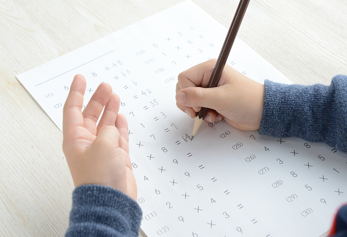 Child holding a pencil in his right hand answering sums on a piece of white paper