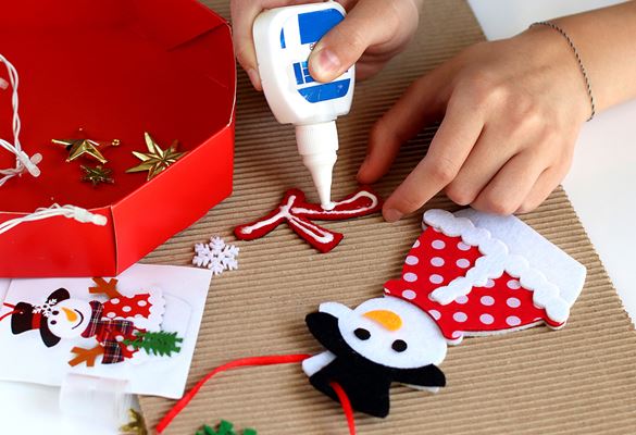 Hand holding glue applying it to a scarf with two cut-outs of snowmen