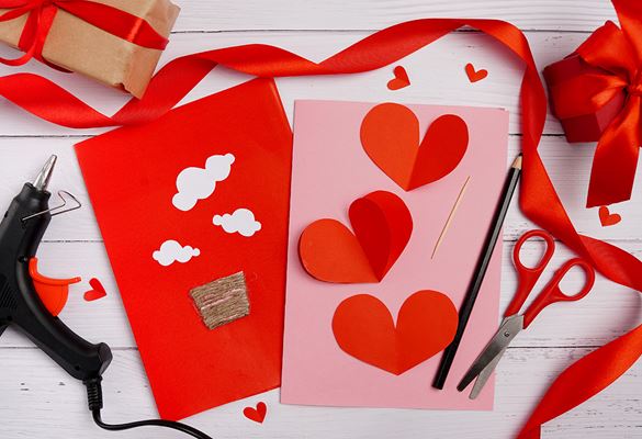 Two cards with hearts surrounded by a pencil, scissors, glue gun and ribbons