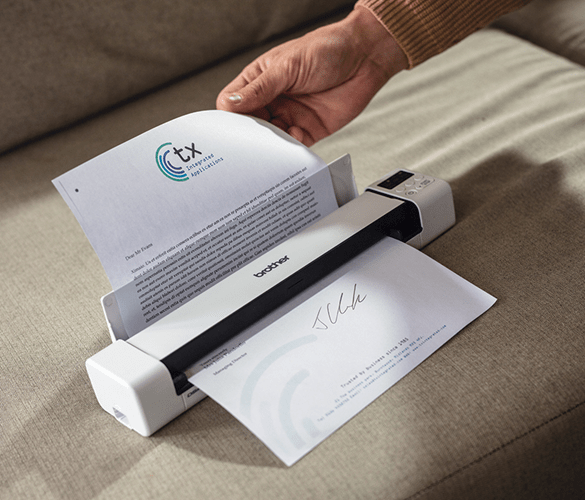 Hand feeding a sheet of paper through a scanner which is placed on a settee