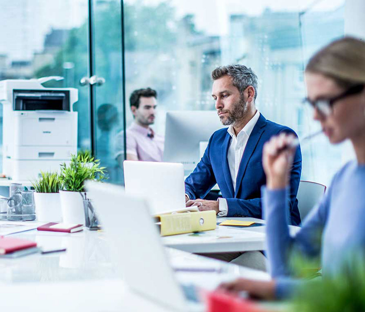 Three people sat at desks in office with a printer