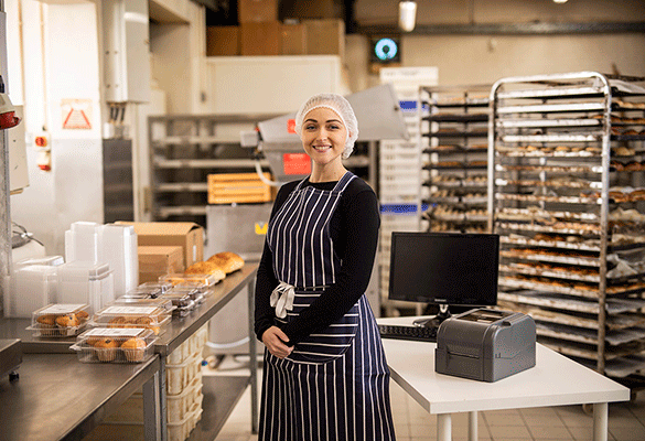 Lady in apron and hair net stood in industrial kitchen next to TD-4T Brother printer