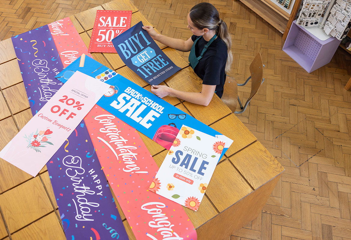 A range of larger format banners on a wooden table, female using laptop