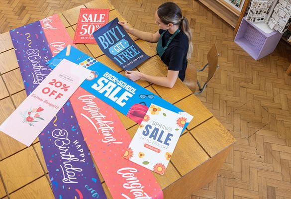 A range of larger format banners on a wooden table, female using laptop