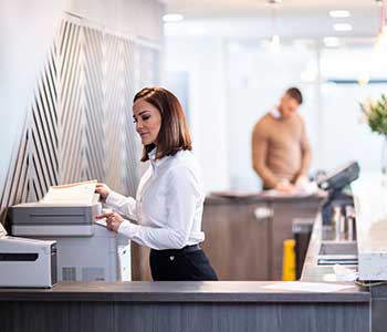 Female wearing white shirt scanning document in reception, man in brown jumper, flowers