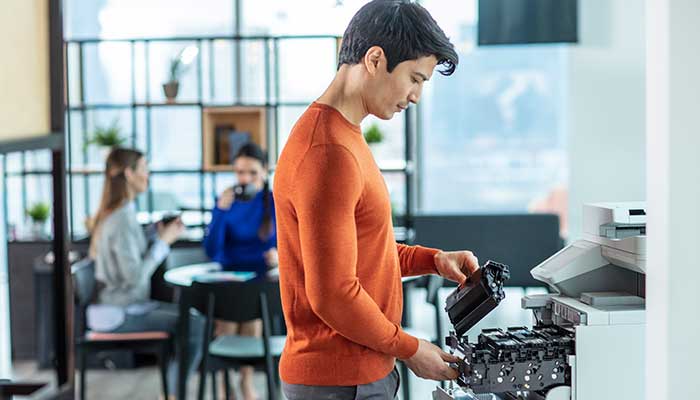 En mann i oransje genser på et kontor setter inn en ny toner i en Brother farge laserskriver