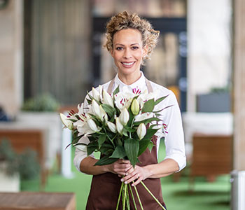 Woman with curly hair tied back with brown apron holding large bunch of flowers