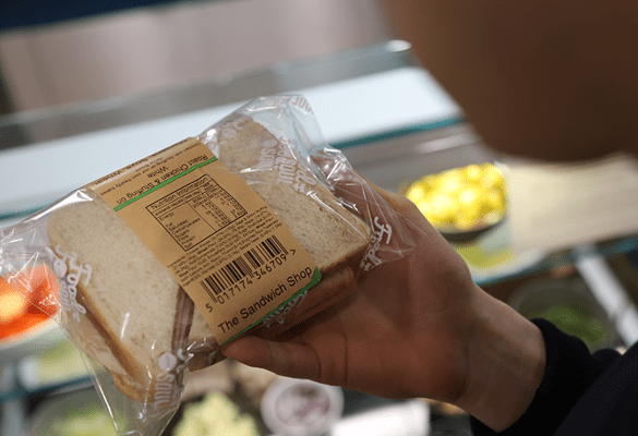 Person holding  sandwich in clear plastic bag with brown label with ingredients