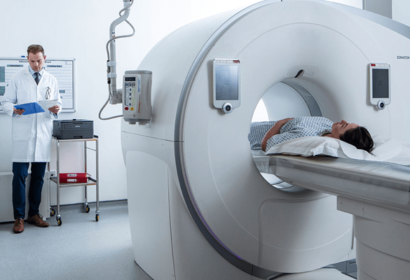 Pacientka v lékařském CT skeneru, doktor v bílém plášti drží modrou složku vedle tiskárny Brother HL-L2370DW