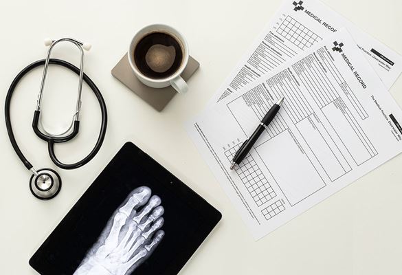 Lekárske dokumenty, pero, šálka kávy, stetoskop, tablet s röntgenom chodidla na bielom stole
