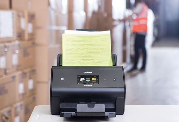 Brother ADS-3600W desktop scanner on table archiving dispatch notes in a warehouse, boxes, man in hi-vis 