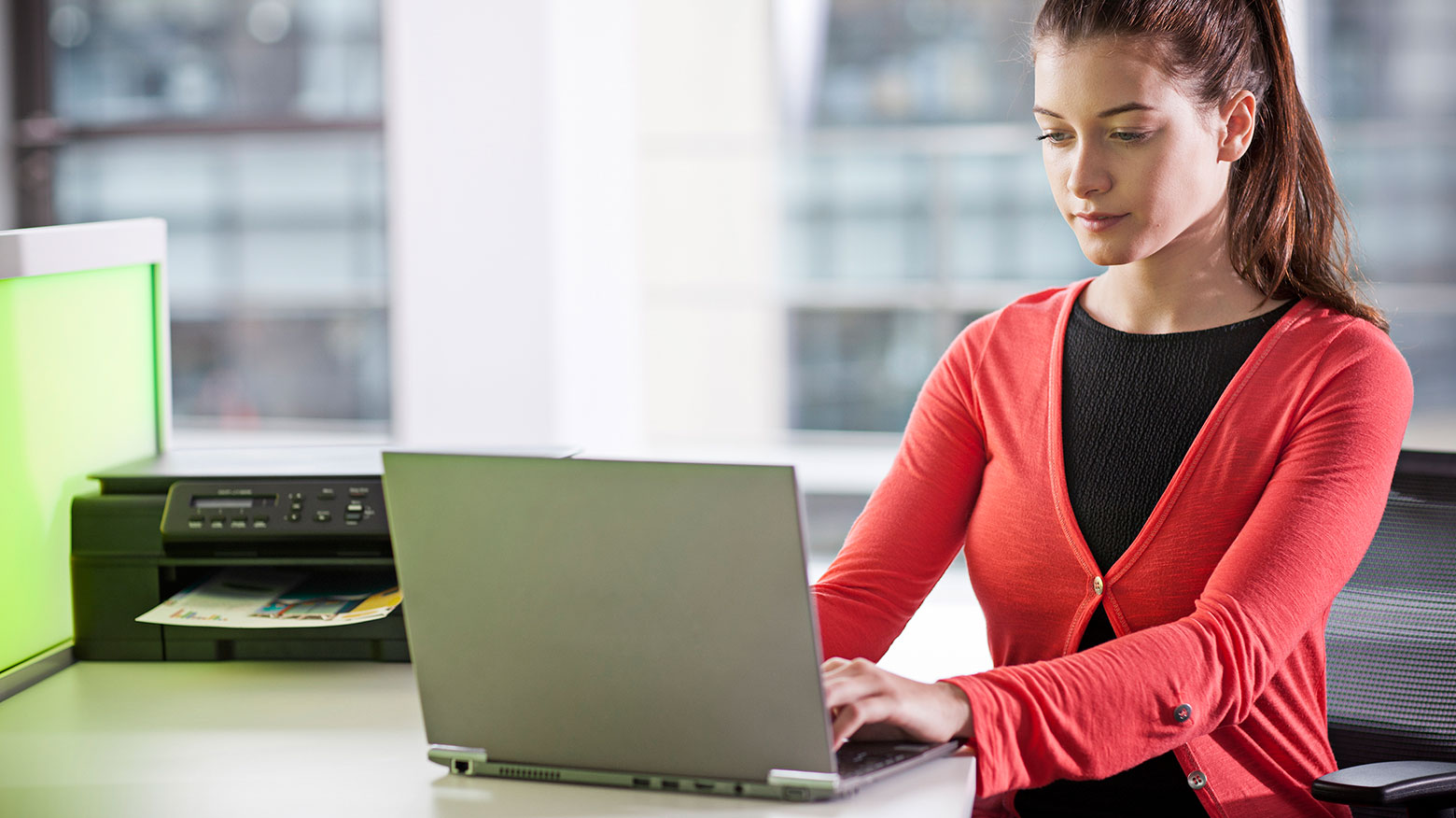 Dame jobber på en laptop på kontoret med en Brother skriver i bakgrunnen