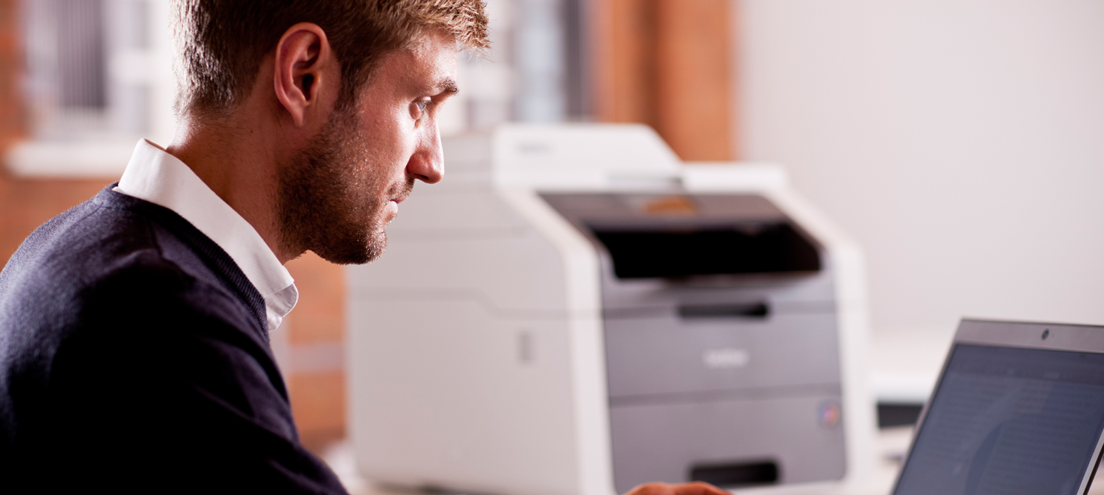 Man on laptop with Brother printer in the background