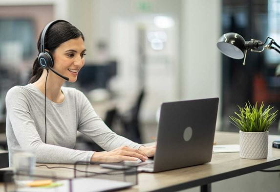 Hymyilevä nainen istuu tietokoneellaan ja juttelee asiakkaan kanssa Brotherin yritysratkaisuista