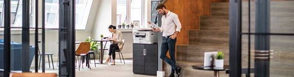 Man stood next to printer on a cabinet, office, tables, plants