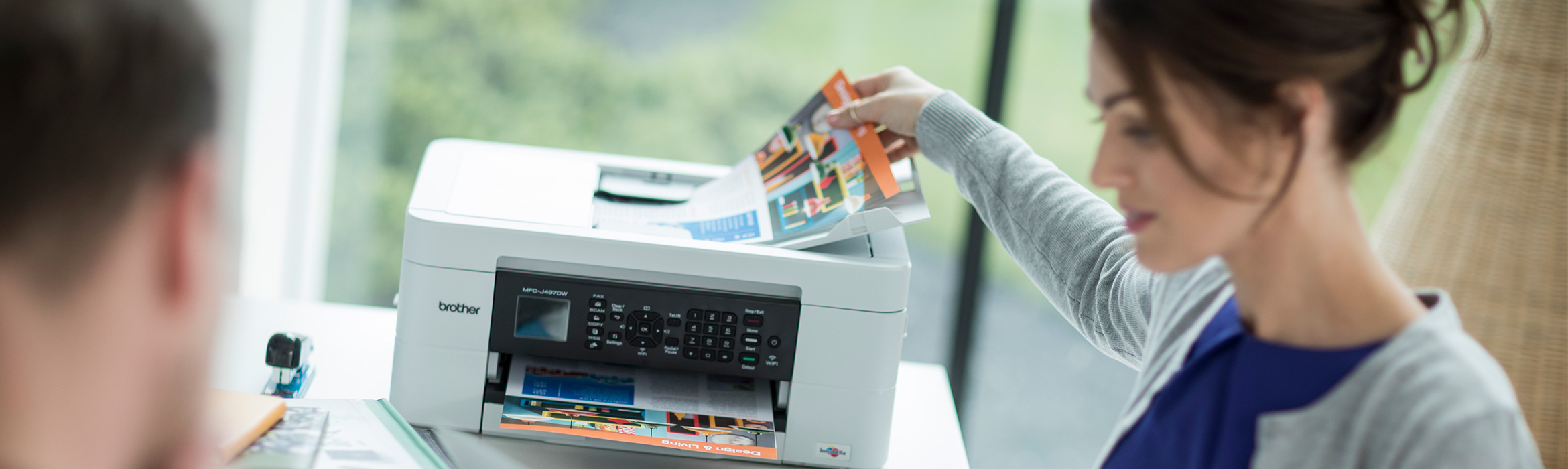 Woman sat at desk picking up document from printer