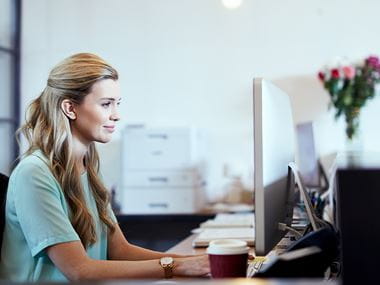 Kvinna sitter vid dator på kontor med skrivare i bakgrunden