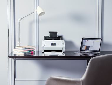 Brother skener na leseni pisarniški mizi z belo svetilko in prenosnikom