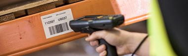 Warehouse racking with Brother thermal label containing a barcode, being scanned with barcode scanner.