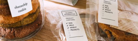 Potravinářské výrobky označené bílými štítky s černým textem informací o alergenech. Řešení pro značení potravin pro kavárny, lahůdky, kuchyně a maloobchody