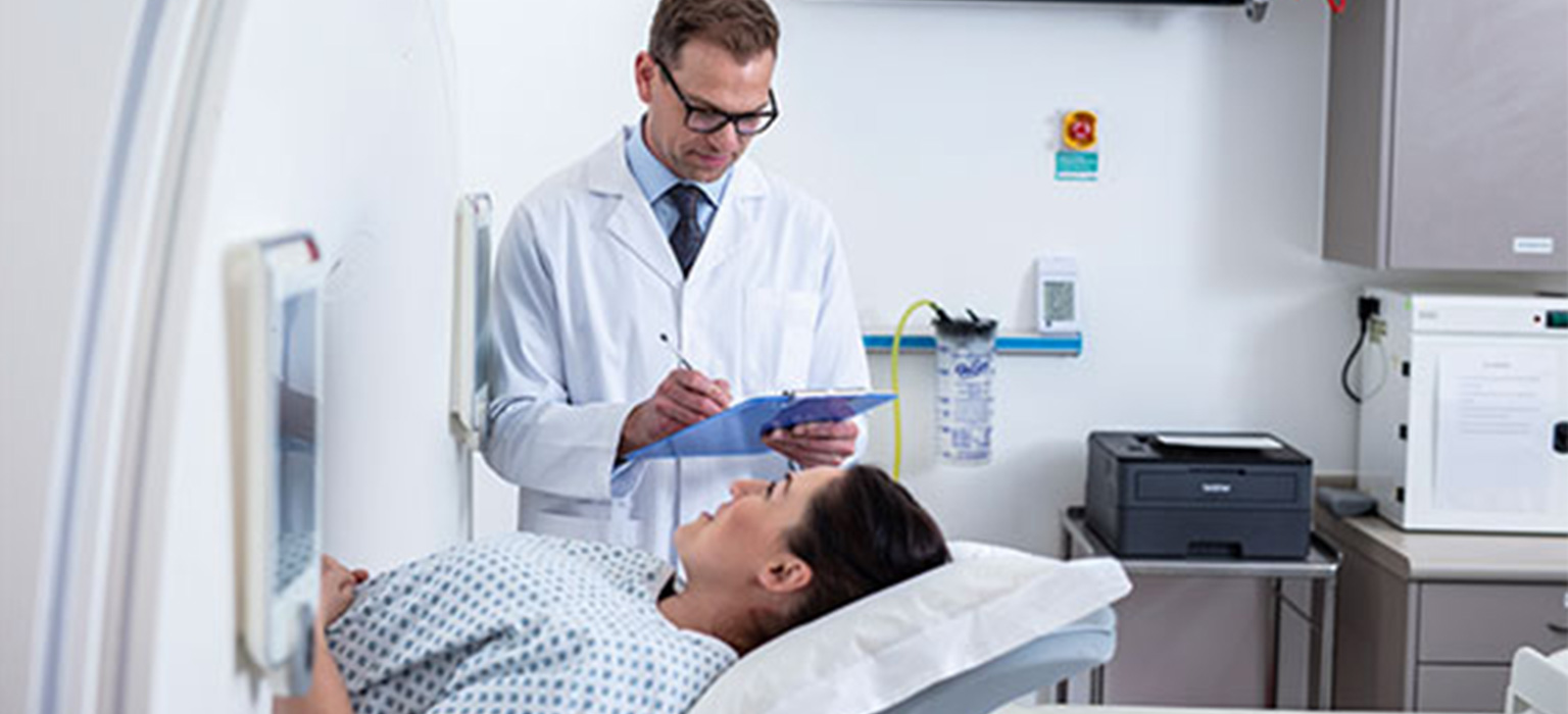 Male doctor in hospital wearing white coat with female patient in CT scanner
