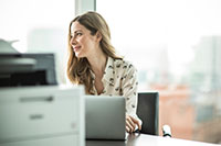 Woman sat at desk with laptop and printer on desk