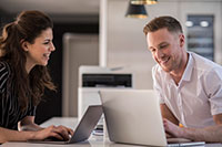 Man and woman sat at desk with printer between them in background