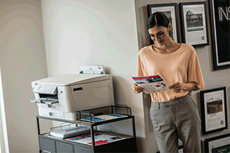 En kvinne på kontoret står ved siden av en Brother blekkskriver med et A4 farge dokument