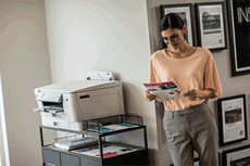 Woman in office next to printer holding A4 colour document