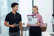 Man and woman holding A3 colour document walking in office